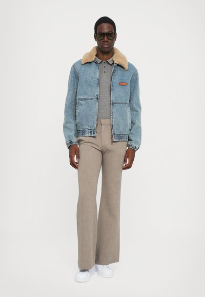 Chaqueta de denim con un cuello de borrego beige, combinada con un polo gris y pantalones de campana beige. Los accesorios incluyen gafas de sol oscuras y zapatillas blancas.