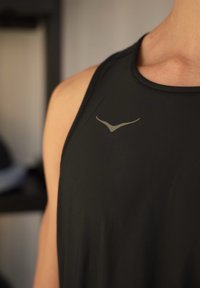 Débardeur de sport noir fabriqué en tissu évacuant l'humidité, doté d'un logo gris subtil et d'une coupe sans manches pour une meilleure ventilation.