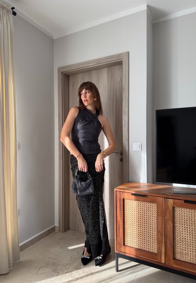 Top ajustado de satén negro con diseño drapeado, combinado con una falda negra con lentejuelas. Los accesorios incluyen un bolso pequeño de cuentas negras y tacones negros.