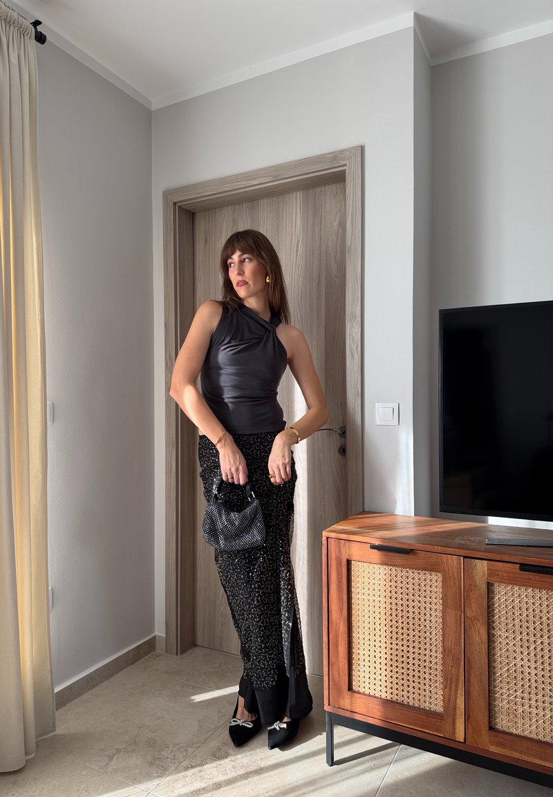 Mustast satiinist kroogitud top koos volditud disainiga, millele on lisatud must lõhikuga sädelev seelik. Aksessuaaridena väike must helmeste kandekott ja mustad kontsakingad.