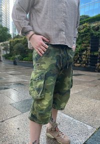 Kamuflaažiga cargo lühikesed püksid, millel on paelaga vöö, kaks külge taskut ja kulunud äärted. Seljas on pruuni värvi spordijalatsid ja ruuduline nööbiga särk.