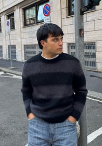 Crno-sivi prugasti džemper s okruglim izrezom, izrađen od mekane tkanine. Uparen s svijetloplavim trapericama. Ležerni urbani ambijent.