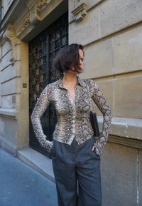 En skjorta med knappar i ormtryck, med långa ärmar och en figurnära design. Kombinationen med grå byxor med hög midja och vida ben samt en liten svart väska.