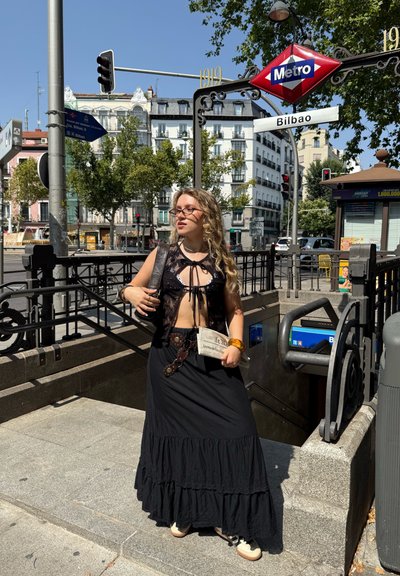 Falda larga negra con capas y dobladillo con volantes, chaleco negro transparente con cierre de lazo, los accesorios incluyen un bolso transparente y una pulsera amarilla.