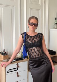 Svart blonde topp med korte ermer, kombinert med et langt, glattes brown satengskjørt. Tilbehøret inkluderer store øreringer og en blå veske med snor.