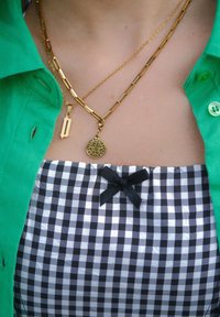 Dve zlate ogrlice, složene na zeleni majici, skupaj z obleko v črno-beli karirici z majhnim črnim zavezovalom.