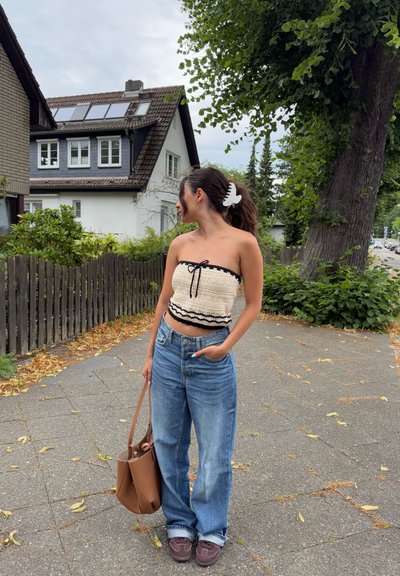 Top sin mangas de ganchillo beige con detalles en negro, jeans livianos de tiro alto en azul claro, bolso tote marrón y zapatos oscuros con detalles de costura.