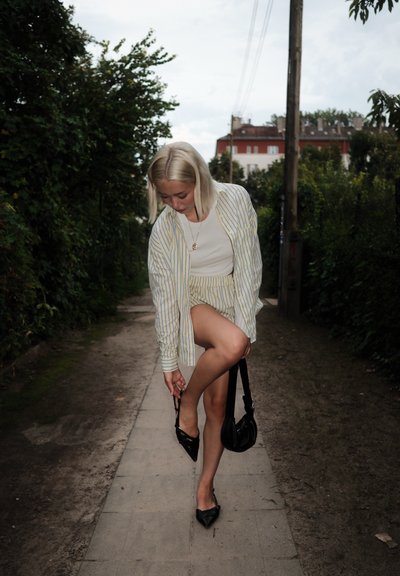 Camiseta blanca combinada con una camisa oversized a rayas azul y amarilla y pantalones cortos a rayas. Bailarinas negras de punta y un pequeño bolso negro.