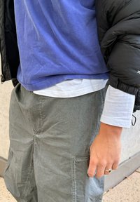 Outfit stratificato composto da una t-shirt in cotone blu, una camicia bianca a maniche lunghe sotto e pantaloni cargo leggeri grigi con texture e tasche.