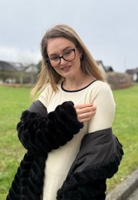 Kremowa bluzka z długim rękawem o prążkowanej strukturze, noszona pod czarnym, obszytym miękkim futrem, oversize płaszczem z obszernymi rękawami.