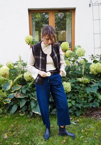 Gilet in misto lana con un motivo a quadri bianco e nero sopra un dolcevita a coste color crema, abbinato a jeans corti blu scuro e stivaletti neri.