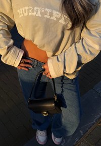 Sweat-shirt beige court avec le texte "MULTIPLY", jean bleu taille haute, sac à main noir et baskets roses et blanches. Manches longues et coupe décontractée.