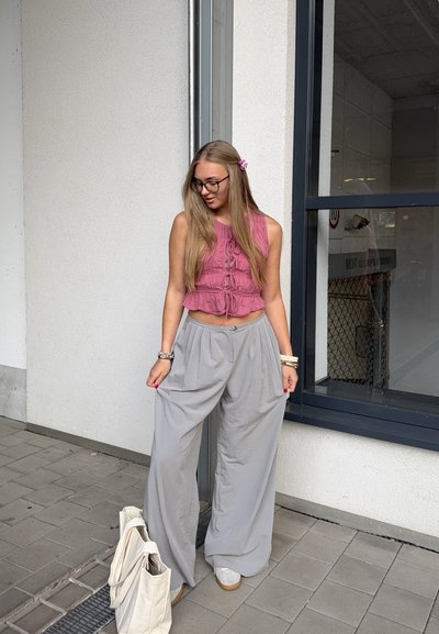 Top corto rosa con lazo delantero y pantalones grises de corte acampanado. Zapatillas blancas y un bolso tipo tote en crema. Cabello largo con un clip de flor.