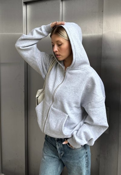 Sudadera gris con cremallera en material de forro polar, con dos bolsillos frontales, combinada con unos vaqueros de tiro alto de color azul claro y un bolso de lado.