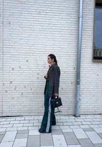 Overdimensjonert grå rutete blazer, grønne bukser med vide ben og hvite striper, svart håndveske. Strukturert vegg og fortau med lysegrå fliser.