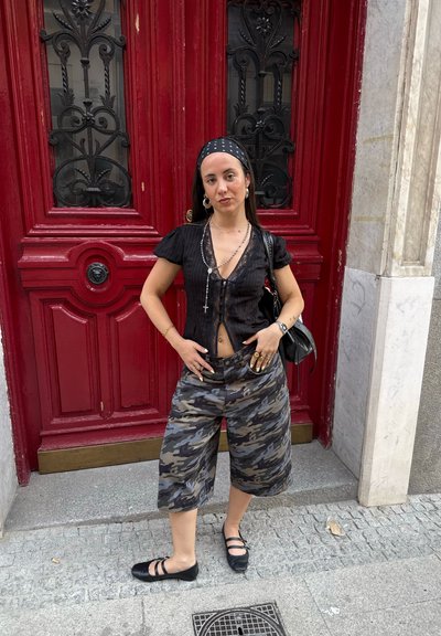 Blusa negra ajustada de manga corta con detalles de encaje, combinada con culottes de patrón de camuflaje. Los accesorios incluyen joyas de plata y un bolso negro.