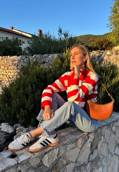 Suéter a rayas rojas y blancas, jeans azul claro con dobladillos deshilachados, zapatillas grises con rayas negras y un bolso de cuero marrón de hombro.