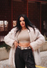 Lichtroze nep bontjas, beige crop top, zwarte high-waisted broek, gemusterd riem met zilveren gesp. Soepele texturen en relaxte pasvorm.