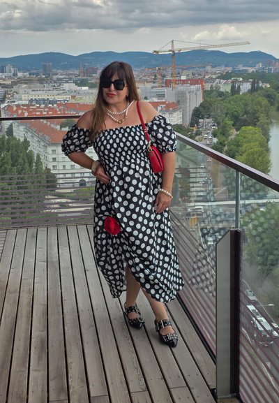 Vestido de lunares en blanco y negro con mangas al hombro, cintura ajustada y acento de rosa roja; combinado con zapatos negros con hebillas.