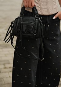 Čierna kožená kabelka s pletenými uchami, predným vreckom na zips, ozdobnými strapcami a striebornými kovaniami. V kombinácii s tmavými denimovými nohavicami so štýlovými grometmi.