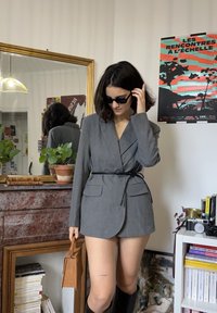 Szara, dopasowana marynarka z paskiem w talii, długimi rękawami i klapami. Do tego kwadratowa torebka i kozaki sięgające kolan. Widoczna faktura tkaniny.