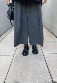 Φαρδιά γκρι παντελόνια από μαλακό ύφασμα, συνδυασμέ�να με μαύρες δερμάτινες μπότες μέχρι τον αστράγαλο, με χοντρή σόλα και ελαστικά στα πλάγια.