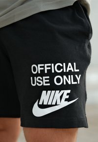 Calções de algodão pretos com o texto branco "APENAS PARA USO OFICIAL" e o logótipo da Nike. O design inclui um corte descontraído e um estilo atlético típico.