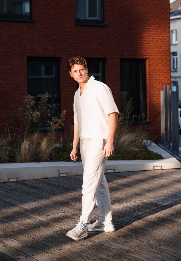 Camisa de lino de color claro con mangas cortas y pantalones a juego con un ajuste relajado; calzando zapatillas blancas; de pie sobre una terraza de madera.