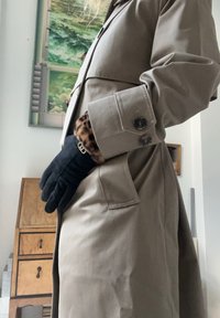 Béžový trenčkot s přiléhavým střihem, s velkými knoflíky, vysokým límcem a detaily leopardího vzoru na manžetách. Přidány černé rukavice.