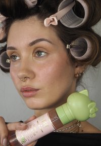 Flacon de brume fixante de maquillage rose avec un capuchon vert en forme de tête de chat. Le flacon présente une texture lisse et un fini brillant.