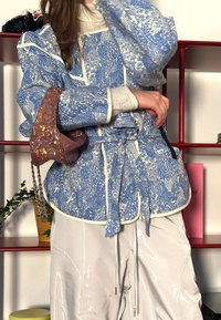 Μπλε σακάκι με σχέδιο και λευκή ρίγα, στενότερο στη μέση, συνδυασμένο με λαμπερό, ανοιχτόχρωμο παντελόνι και μια σπορ τσάντα με υφή και �λάμψη.