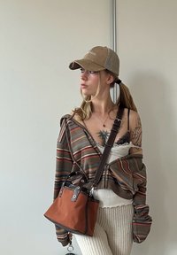 Randig hoodie i jordnära färger, tanktop med spetsdetaljer, ribbade krämfärgade byxor och brun crossbody-väska med svarta accenter.