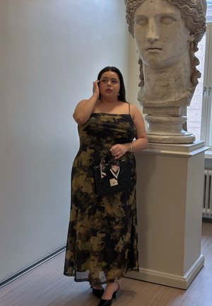 Vestido maxi con estampado de camuflaje, con tirantes de espagueti y tela fluida; combinado con un bolso acolchado negro con acentos florales.