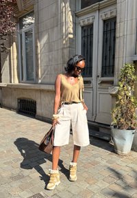 Bolso tote marrón, blusa de satén dorado claro con un detalle de lazo, pantalones cortos anchos color crema y zapatillas altas beige con acentos de camuflaje.