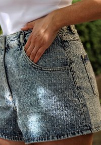 Denim hlače kratke svetlo modre barve z teksturiranim vzorcem, ki vključujejo poškodovane detajle in stranske žepke, z oprijetim dizajnom z visokim pasom.