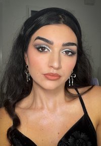 Svart fløyels topp med blomstermønster, sølvøreringer og metallisk øyemakeup med blå accenter. Glatt hud og glansfulle lepper.