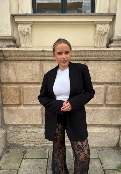 Blazer negro de gran tamaño sobre una blusa blanca, combinado con pantalones de encaje negros. Tejido suave, forma estructurada y patrón de encaje intrincado.