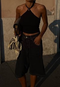 Fekete pántos crop top, laza fekete farmer culotte, barna táska a kezében, és mintás sál, minimalista textúrákkal és kiegészítőkkel.