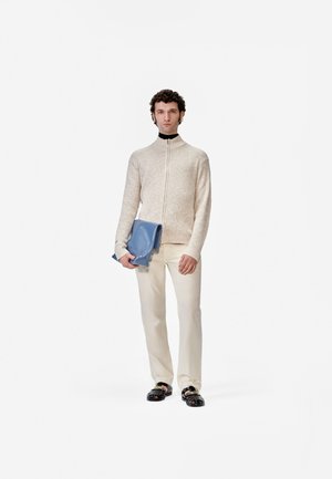 Suéter de punto beige con cremallera, pantalones crema, sandalias negras, sosteniendo un bolso azul brillante. Diseño sencillo con punto texturizado.