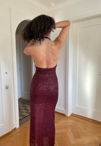 Burgundi színű, flitterekkel d�íszített ruha, testhez simuló sziluettel, hát nélküli kialakítással és földig érő szegéllyel. A sima textúra fokozza a flitterek csillogását.