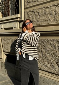 Μαύρη και άσπρη ριγέ υπερμεγέθη πλεκτή μπλούζα, λευκό πουκάμισο από κάτω, μαύρη τζιν φούστα με μπροστινές σχισμές και υπερμεγέθη γυαλιά ηλίου.