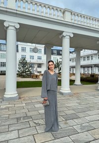 Γκρι πλεκτό σετ πουλόβερ και φούστα, με μακριά μανίκια, μπλούζα σε σχήμα V, ρέουσα σιλουέτα, συνδυασμένο με μια μικρή γκρι τσάντα. Ξεροί βράχοι.