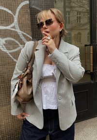 Grå rutmönstrad kavaj bärs över en vit elastisk blus, i kombination med mörk denim, en brun läderväska och stylad med accessoarer.