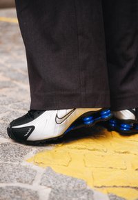 Nike-sneakers hebben een zwart-wit ontwerp met blauwe accenten en een gestructureerde zool. De schoenen hebben een gestroomlijnde vorm en een herkenbaar logo.