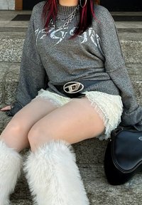 Grijze oversized trui met lange mouwen, witte shorts met kantafwerking, witte fluffy laarzen en een zwarte riem met een glanzende zilveren gesp. Zwarte tas.
