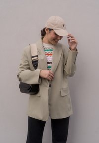Blazer oversized bege, suéter de malha com riscas multicoloridas, mala preta e boné bege. Textura suave, fecho com um botão, dois bolsos.
