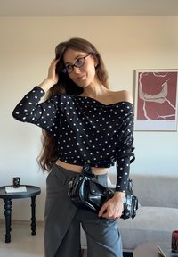 Czarna bluzka z odkrytymi ramionami w białe kropki, zestawiona z szarymi spodniami. Akcesoria to mała czarna torebka z wieloma kieszonkami.