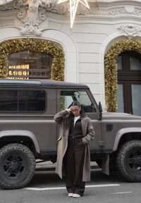 Véhicule utilitaire sport vintage gris garé le long d'une rue ; orné de décorations de vacances dorées ; une personne en manteau et pantalon marron se tient à proximité.