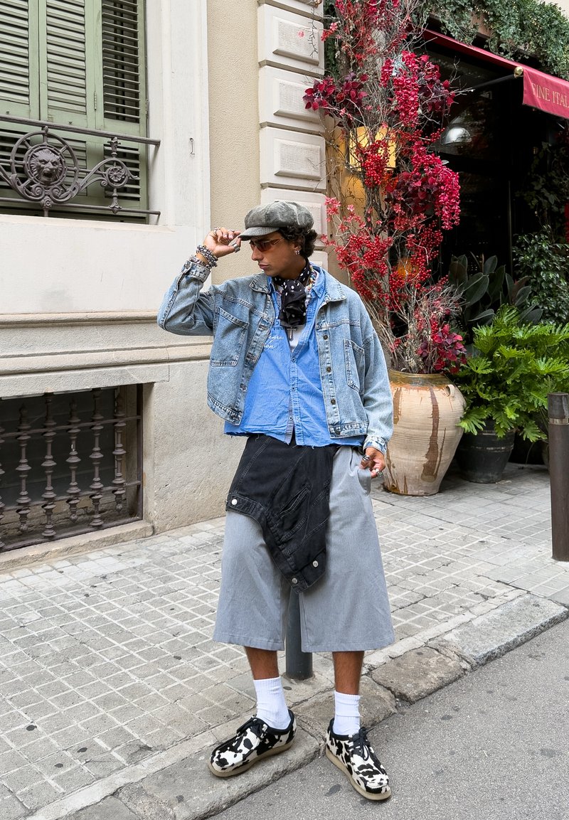 Veste en denim sur une chemise bleu clair, jupe grise et salopette noire courte. Chaussures à motifs noir et blanc avec des chaussettes blanches. Accessoirisée avec une écharpe.