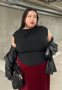 Fekete, rövid ujjú testhezálló felső, hozzáillő, folyékony anyagú bordó szoknyával. Egy fekete bőrdzseki egyik karon lóg, kiegészítve egy kézitáskával.